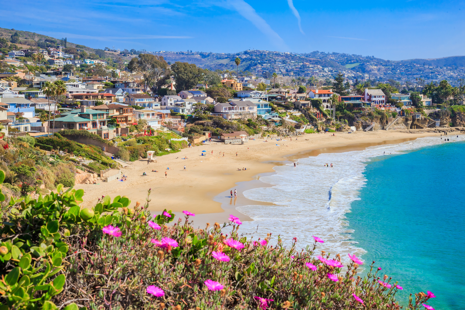 A shot of a beach in Orange County with houses on the hills.