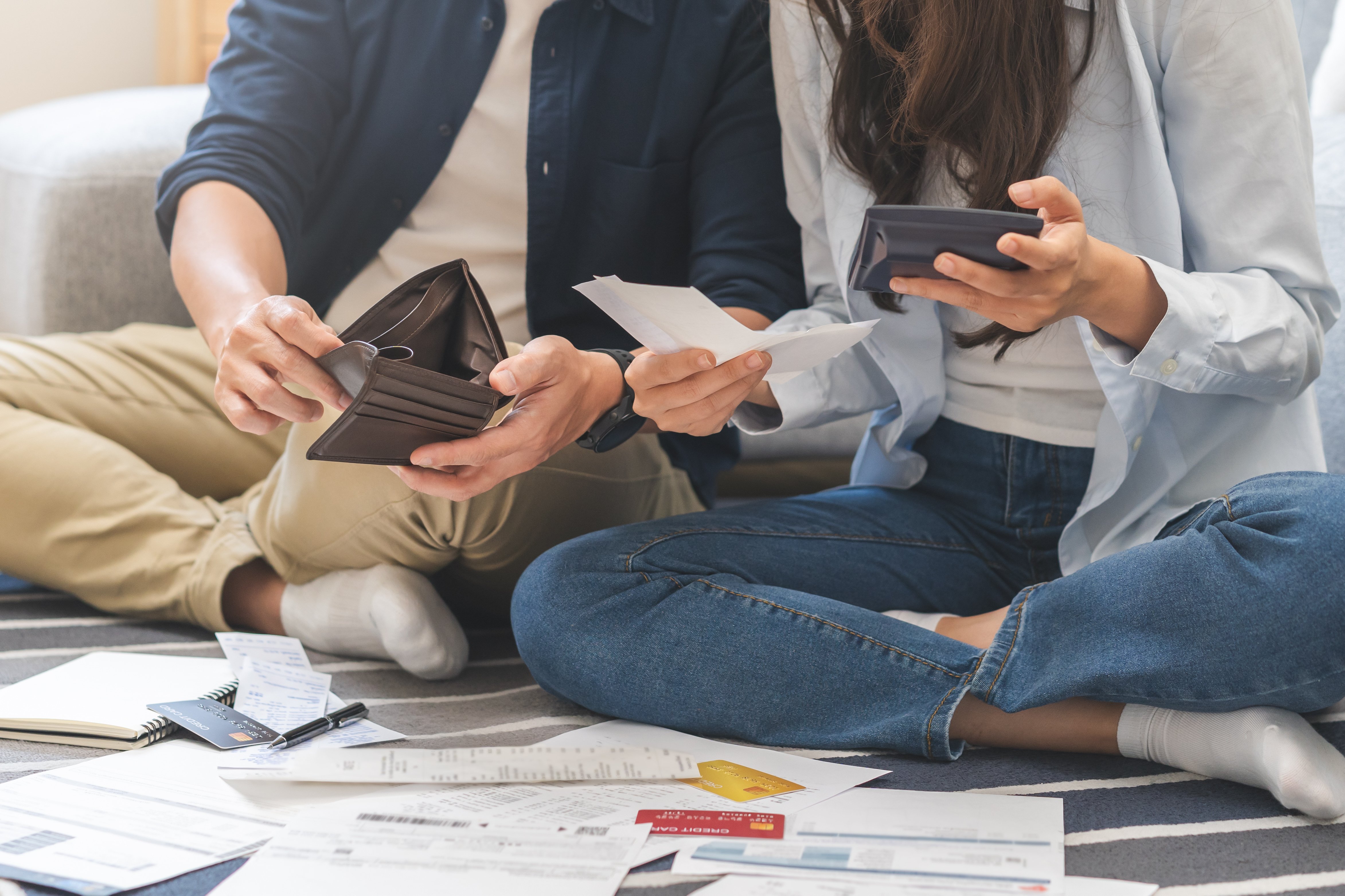 A couple sitting down with financial statements on the ground and wallets in hand