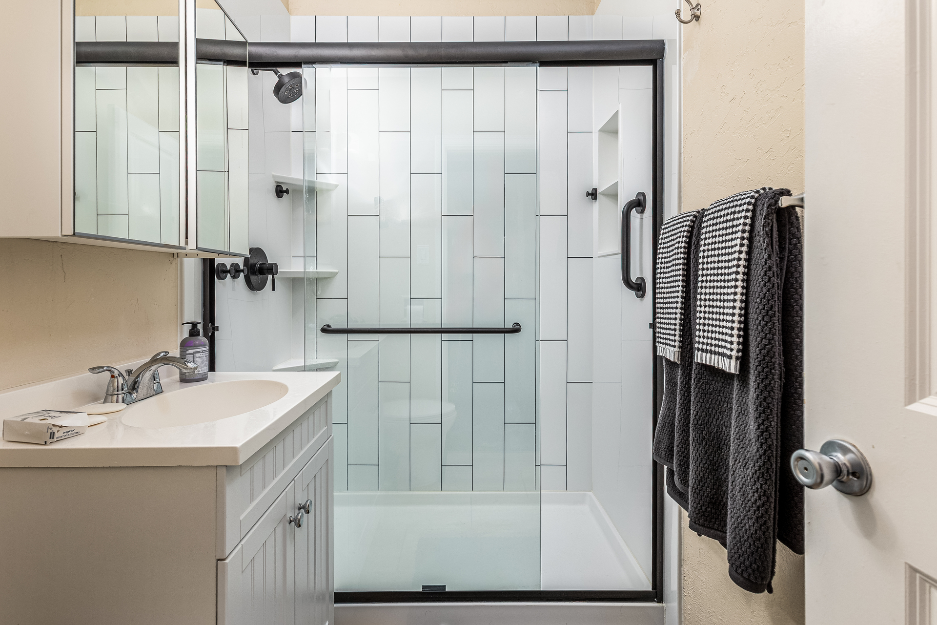 A new walk-in shower remodel with clear sliding glass doors, a grab bar, a shower niche, and 3 corner storage shelves.