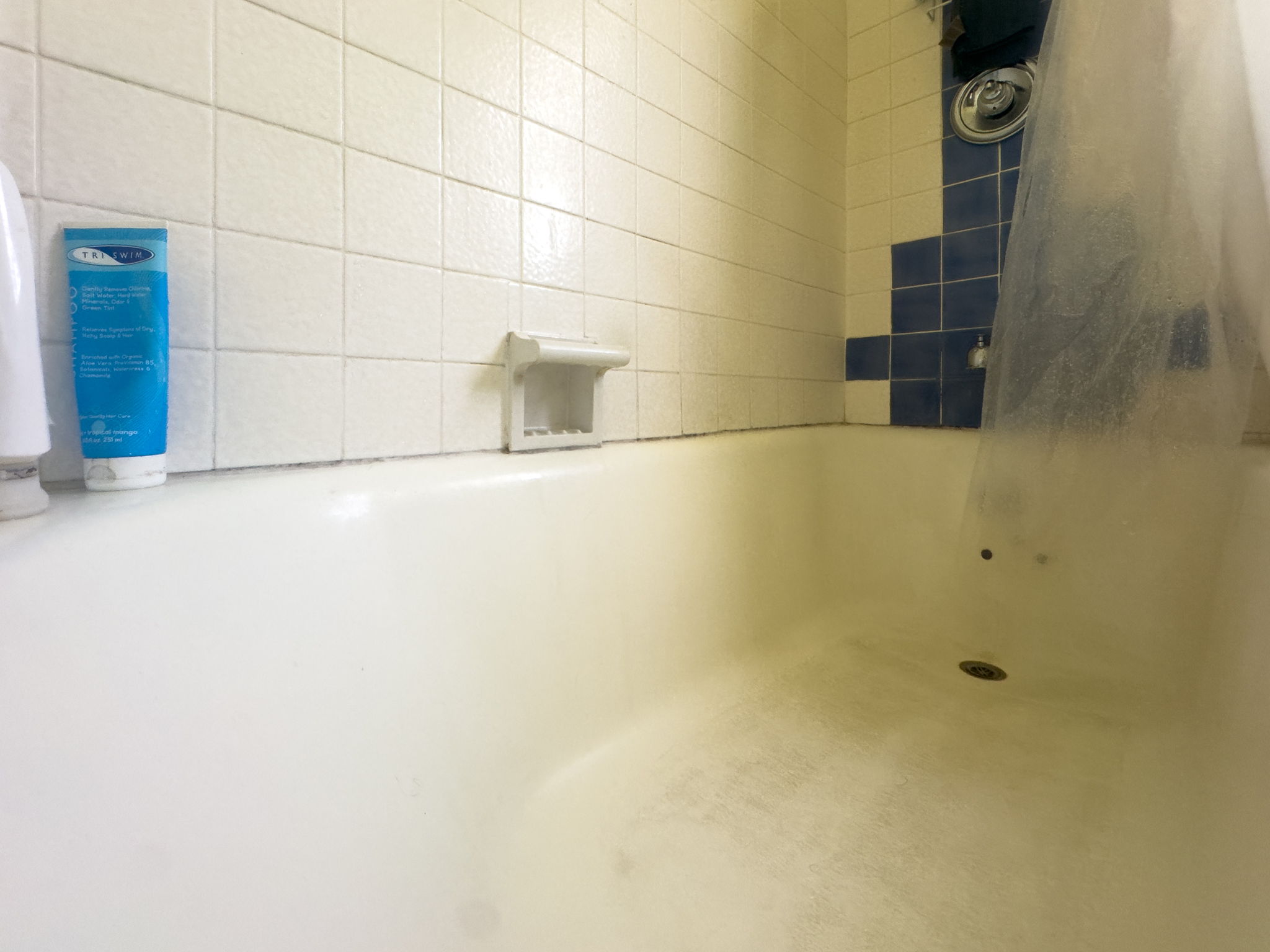 Inside a bathtub with missing silicone, old tile, and a dirty base 
