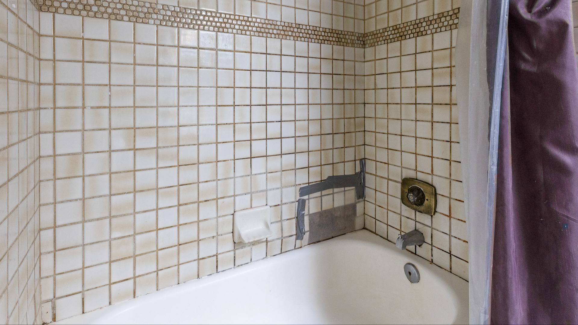 A tile shower with duct tape over a portion of the wall to keep moisture from reaching behind the wall.