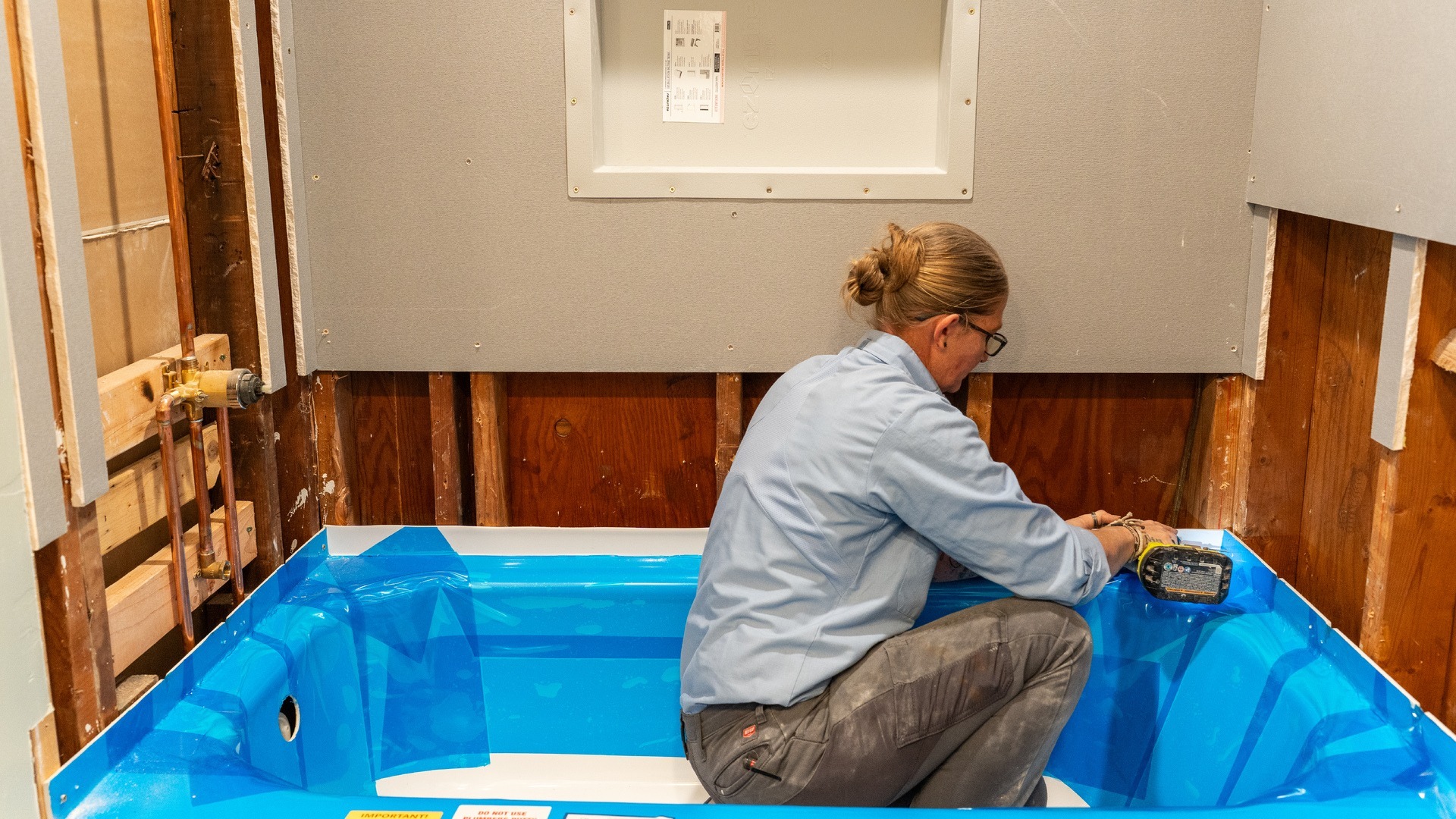 A shower installer uses a power drill to make sure a new tub is put into the shower area correctly.