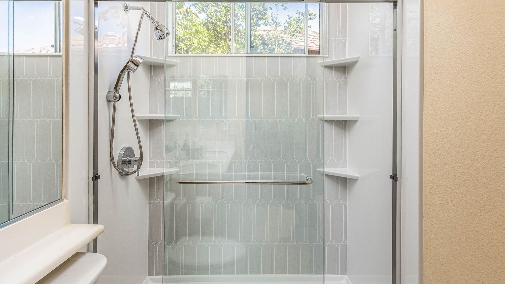 A large walk-in shower with overhead and handheld showers, sliding glass doors, and six corner shelves