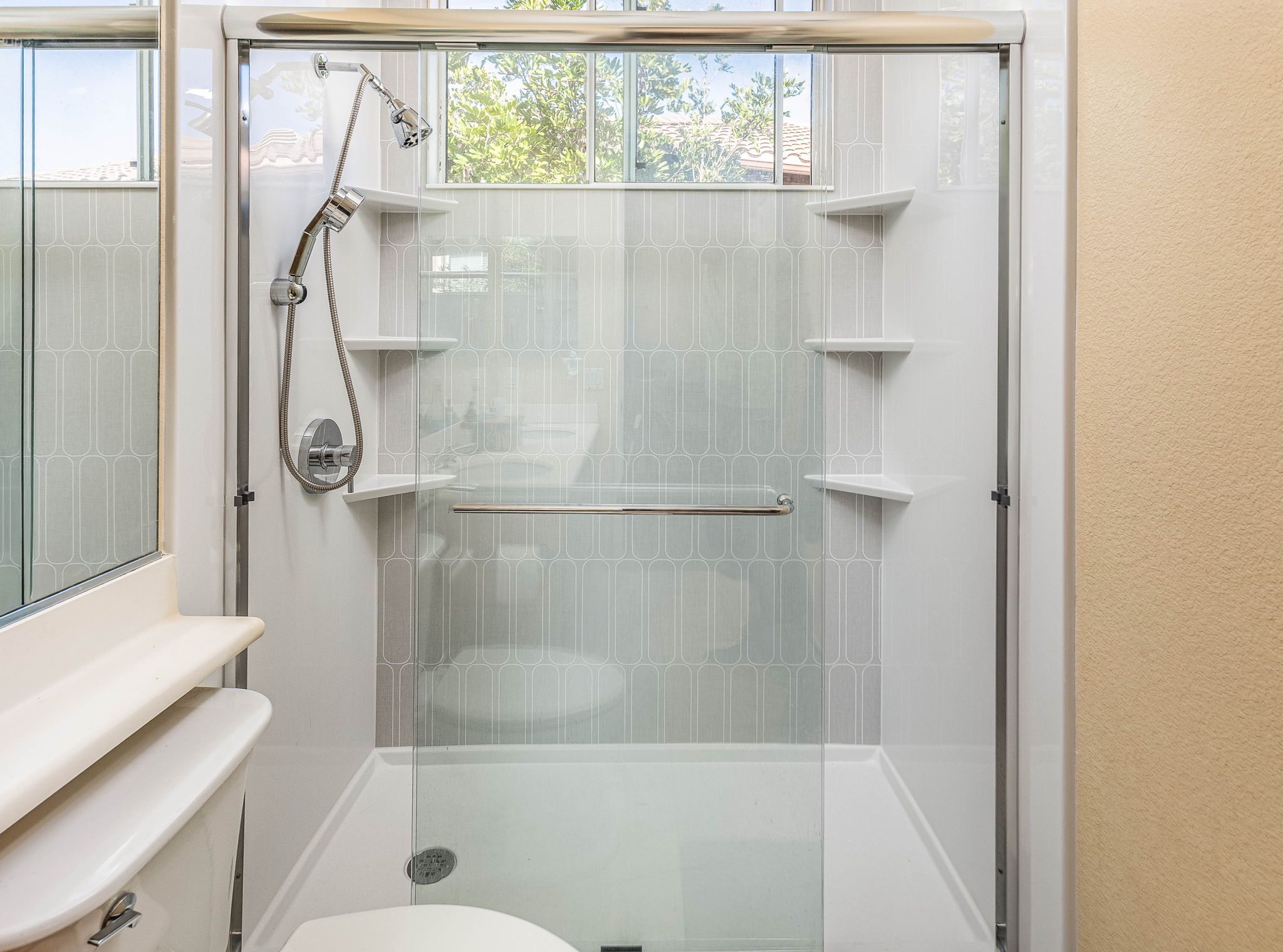 A large walk-in shower with overhead and handheld showers, sliding glass doors, and six corner shelves