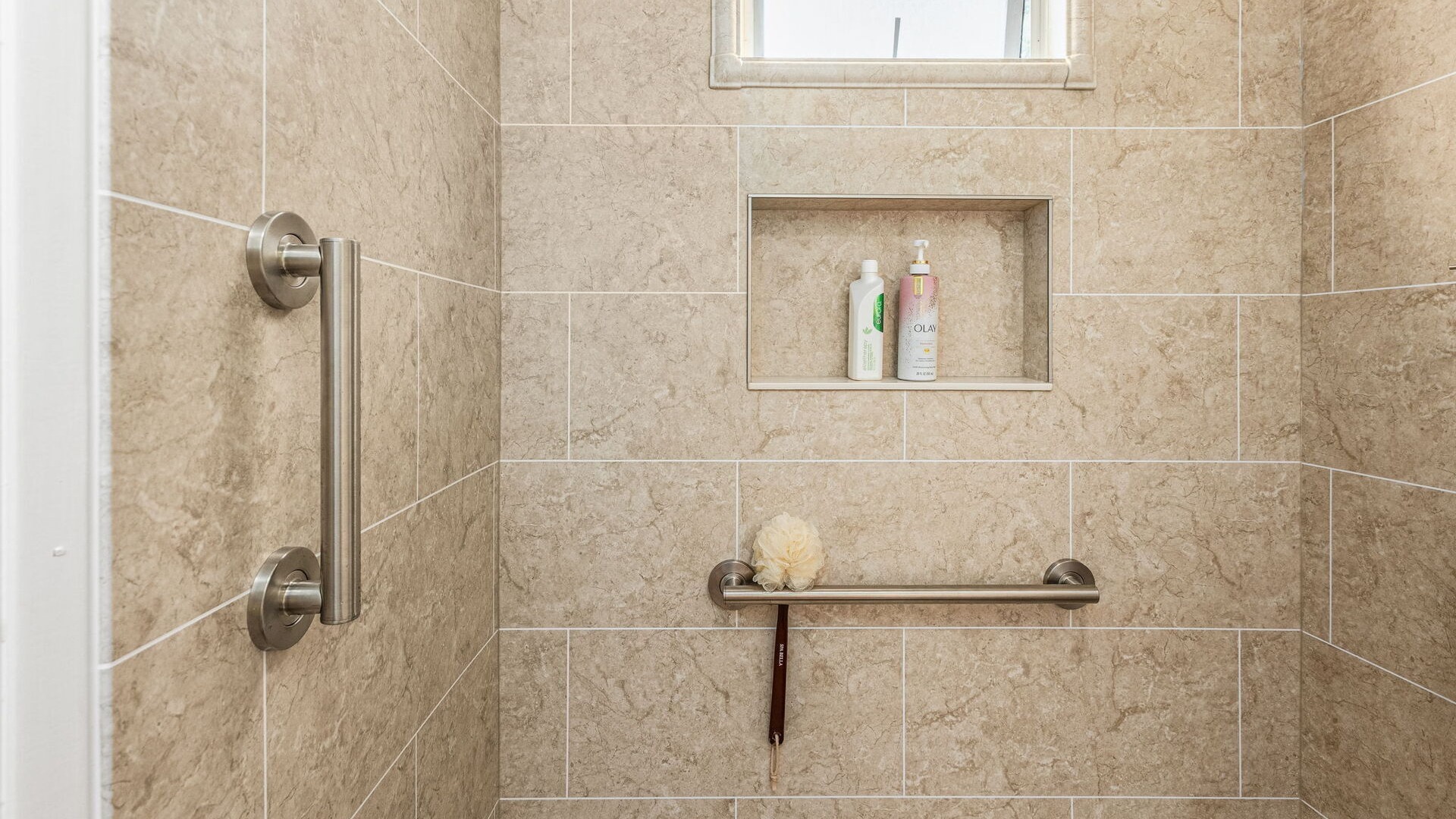 A remodeled shower area with tile-pattern walls, a storage niche with two bottles in it, and two grab bars.