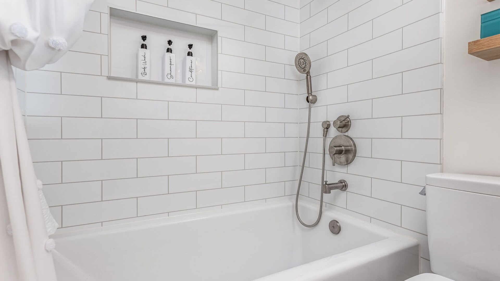 A remodeled shower-tub combo with tile-pattern walls, a handheld shower, and a storage niche with three shampoo bottles.