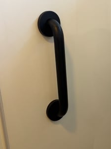 A matte black grab bar attached to a white shower wall.