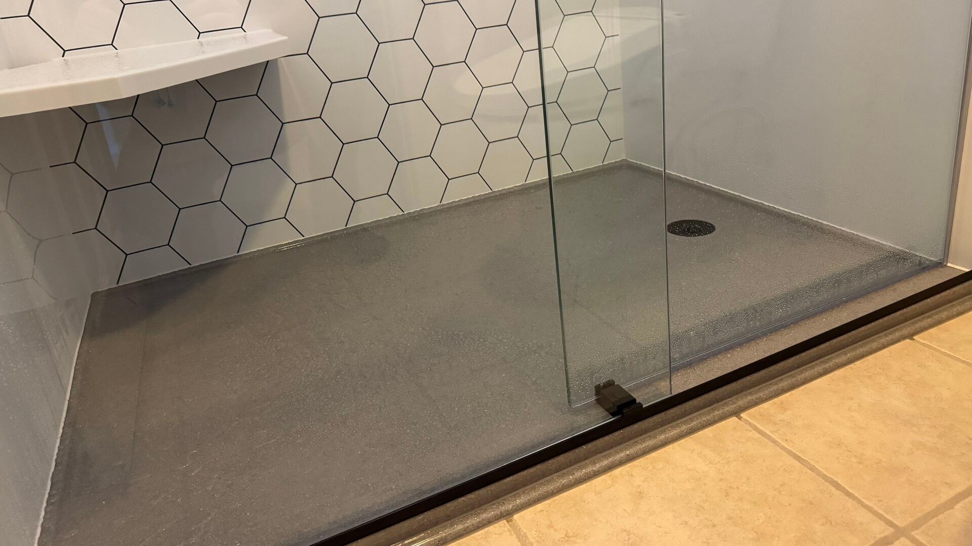 A newly remodeled walk-in shower with a hex pattern accent wall, a corner shower seat, and an onyx shower base.