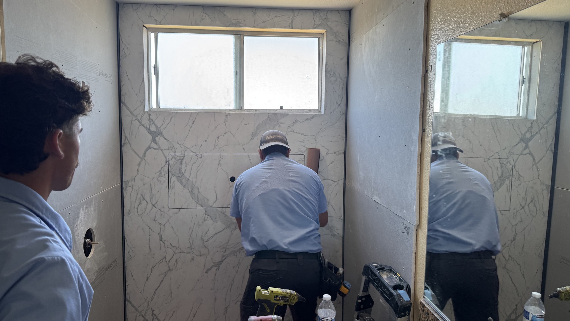 A shower installer and installer assistant putting up shower walls.