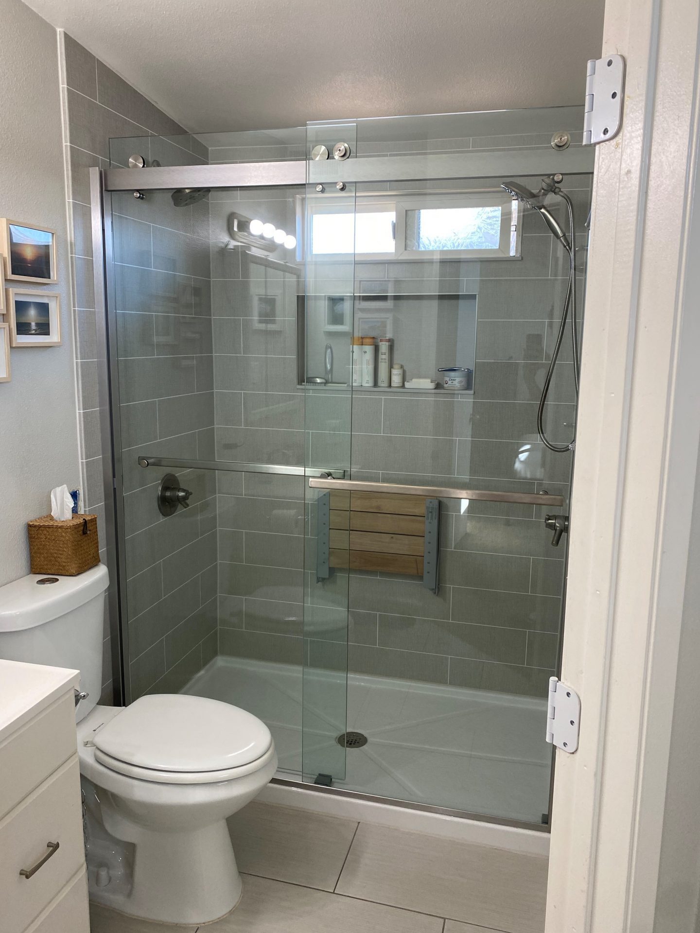A walk in shower with a sliding glass door, a seat for the shower, and a shower storage niche