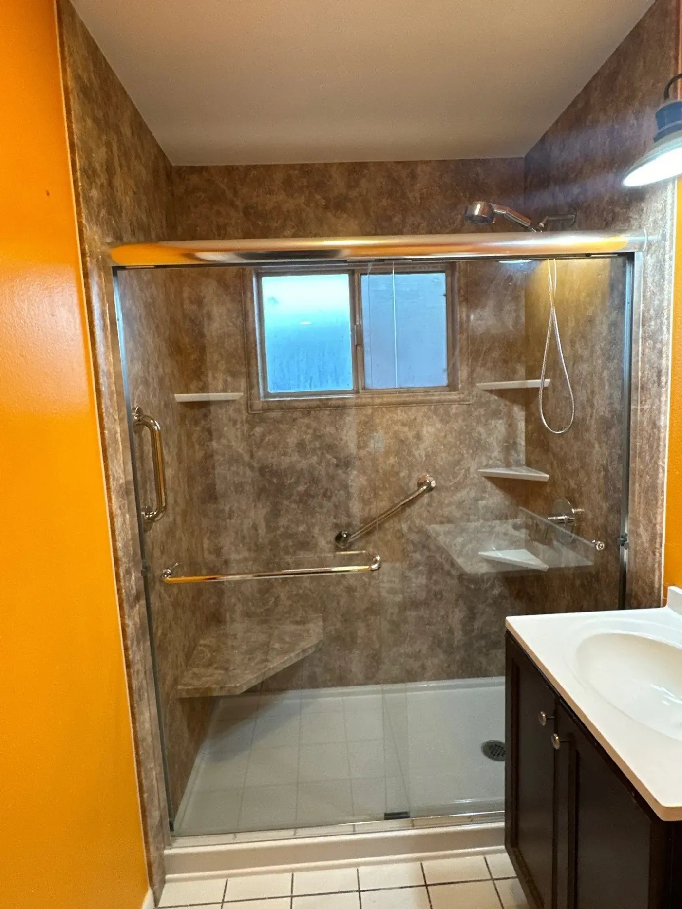 Walk in shower with glass doors, two grab bars, one seat, and four shower storage corner shelves