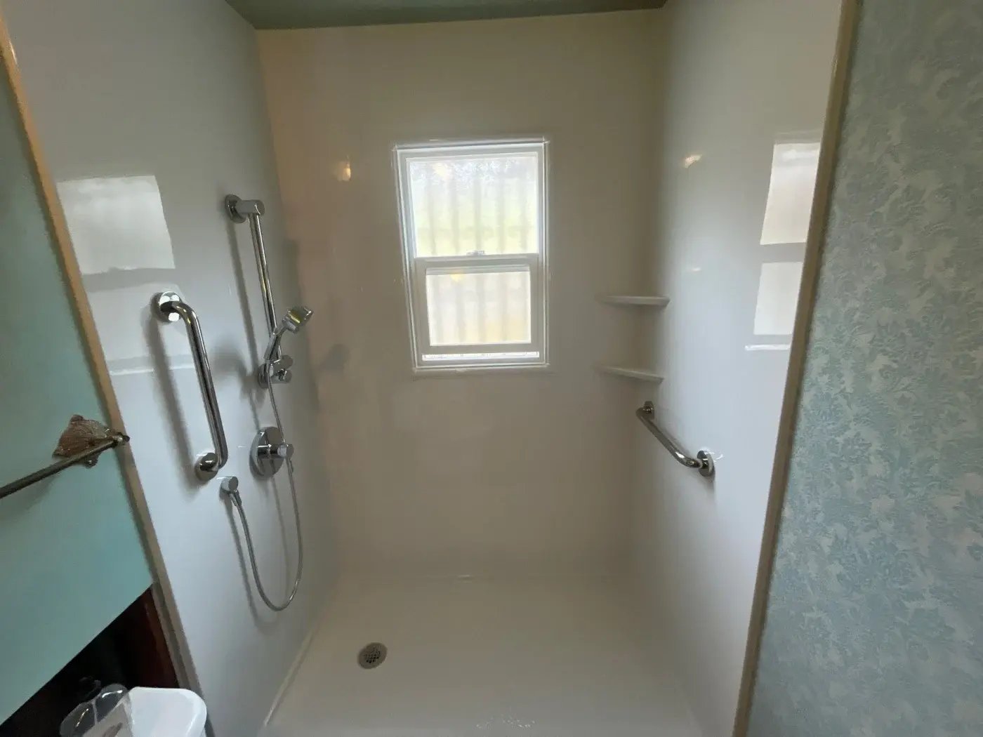 A remodeled shower with two grab bars and two corner storage shelves