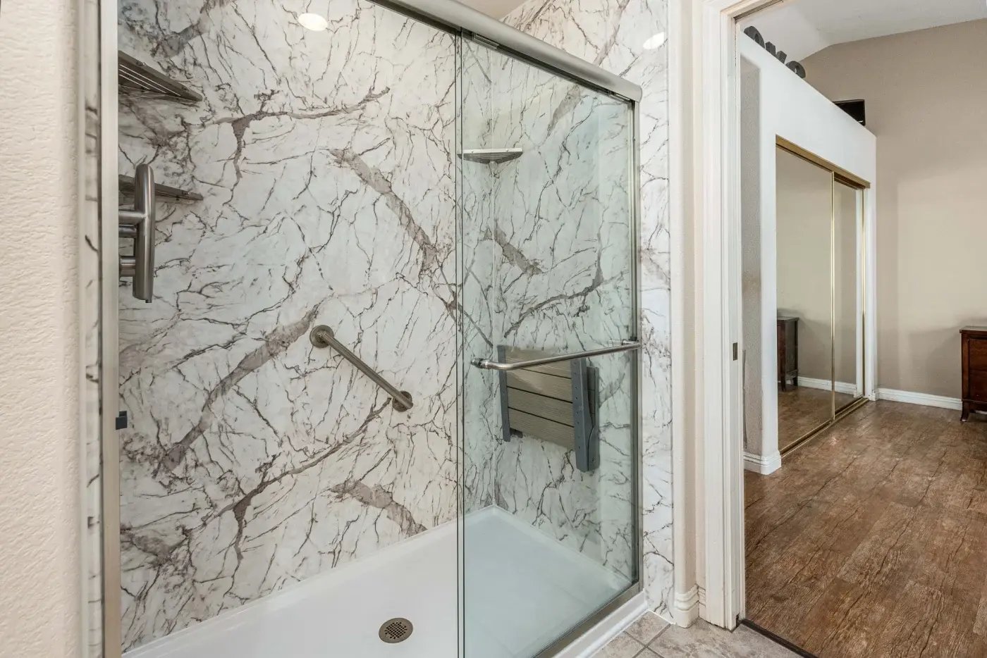 A remodeled shower with a grab bar, shower corner storage, a shower seat, and a sliding glass shower door