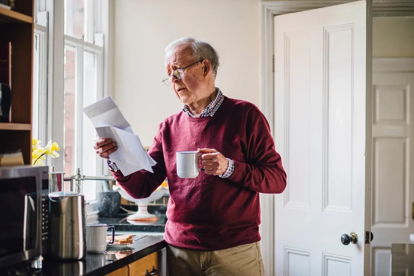 An elderly man with coffee while reading something on a piece of paper 