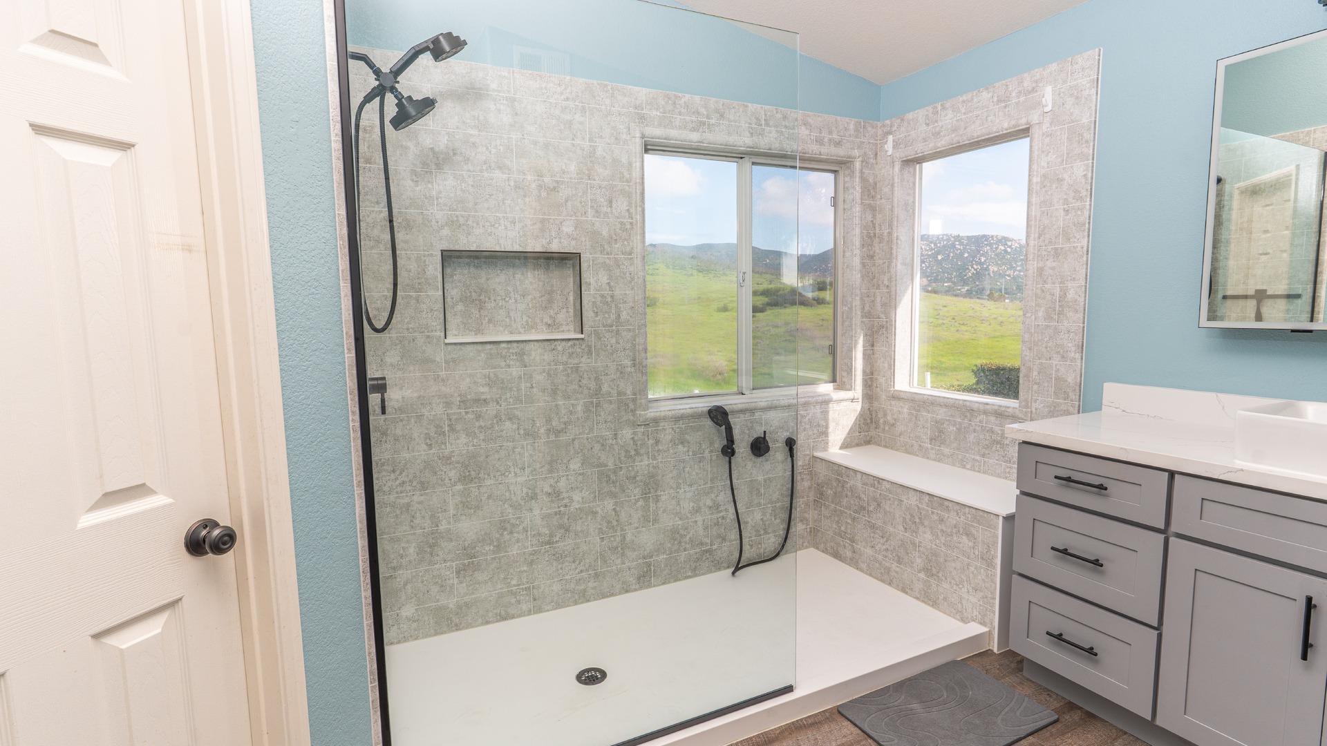 A new walk-in shower with a handheld shower next to a custom seat, a storage niche, and a handheld-fixed showerhead combo on the other side.