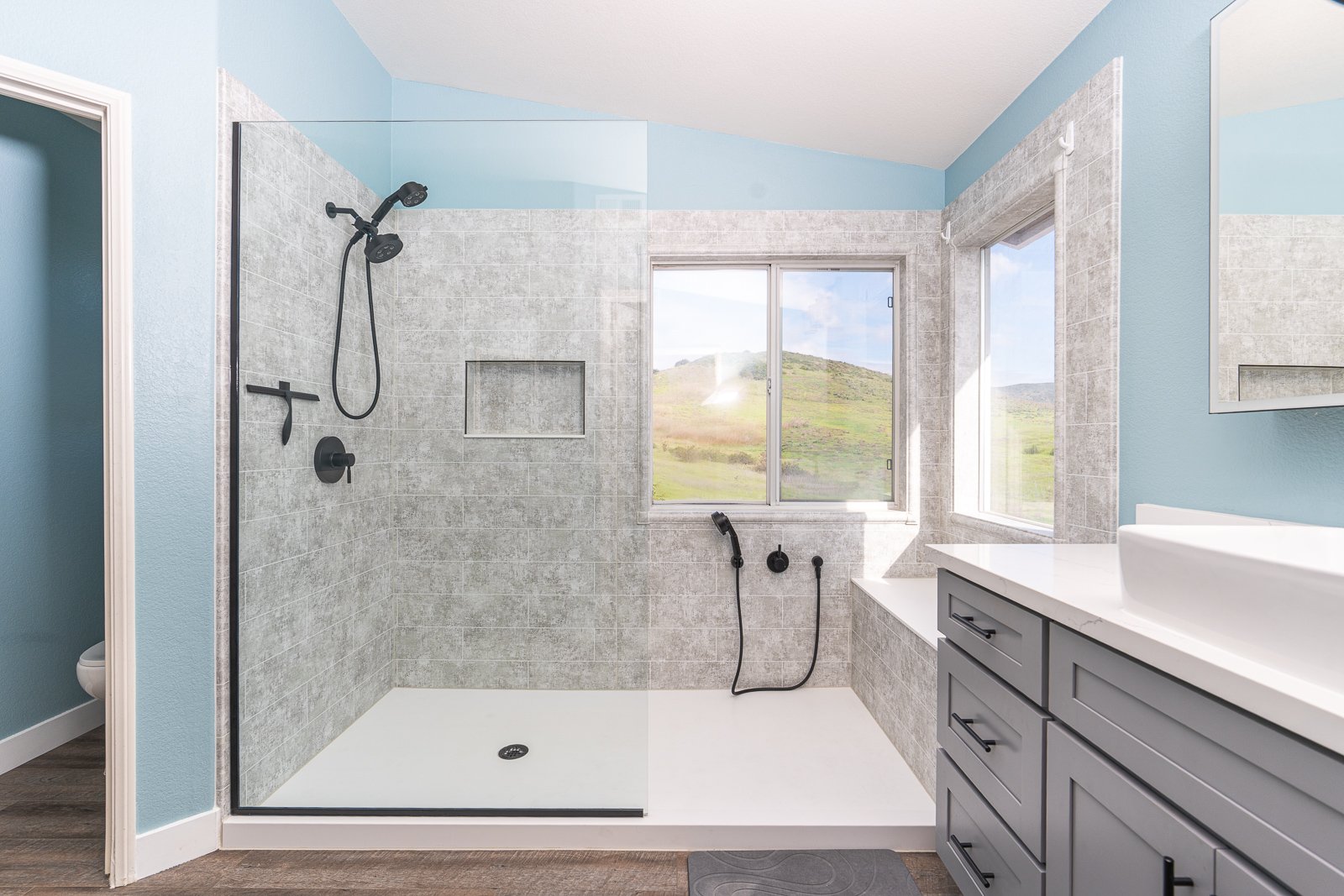 A large walk-in shower with two handheld showers, one fixed shower head, a storage niche, and a custom bench