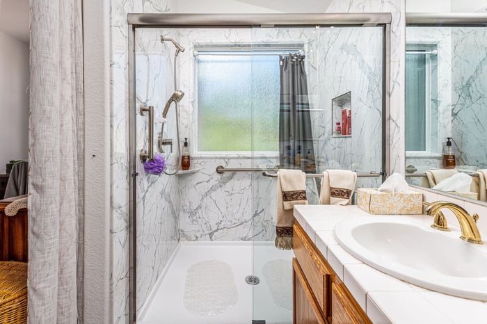 A large shower remodel with Calcutta marble walls, a storage niche, clear glass doors, and two shower heads