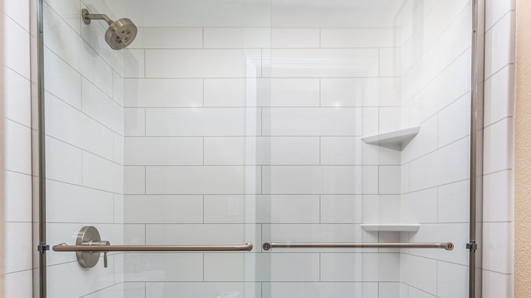 A tile-looking walk-in shower with a fixed shower head and two corner shelves.