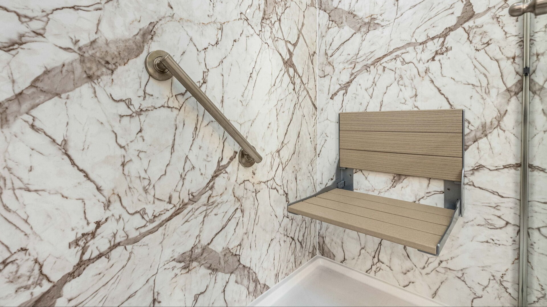 A walk-in shower with a grab bar and a folding shower seat.