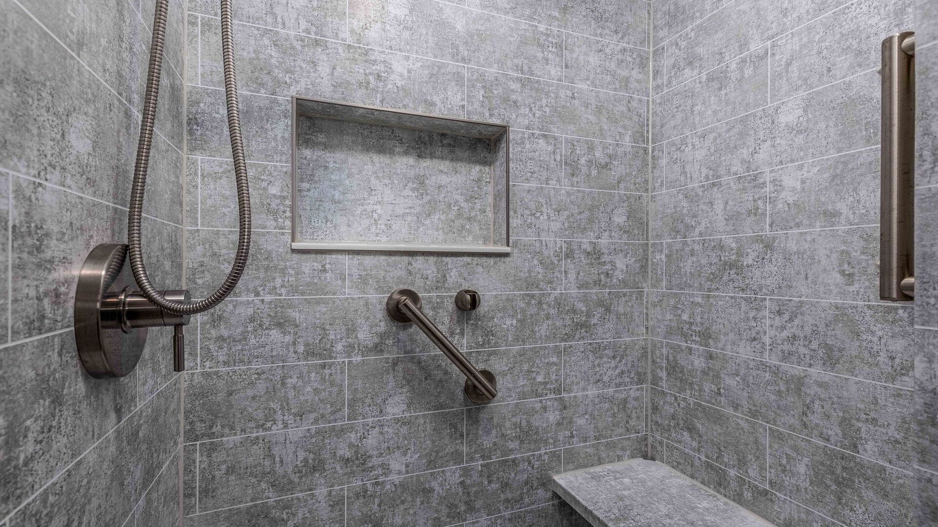 A walk-in shower with a storage niche, two grab bars, and a shower bench.