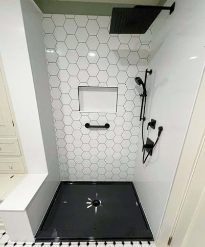 A walk-in shower with a hexagonal pattern accent wall, a shower niche, a black onyx shower base, a handheld shower, and a grab bar.