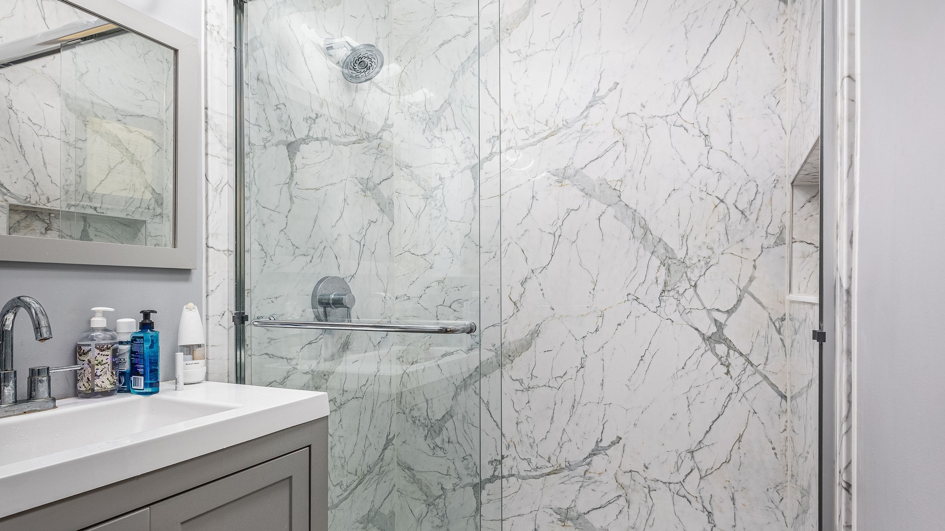 A Calcutta marble walk-in shower with a shower storage niche and a fixed shower head.