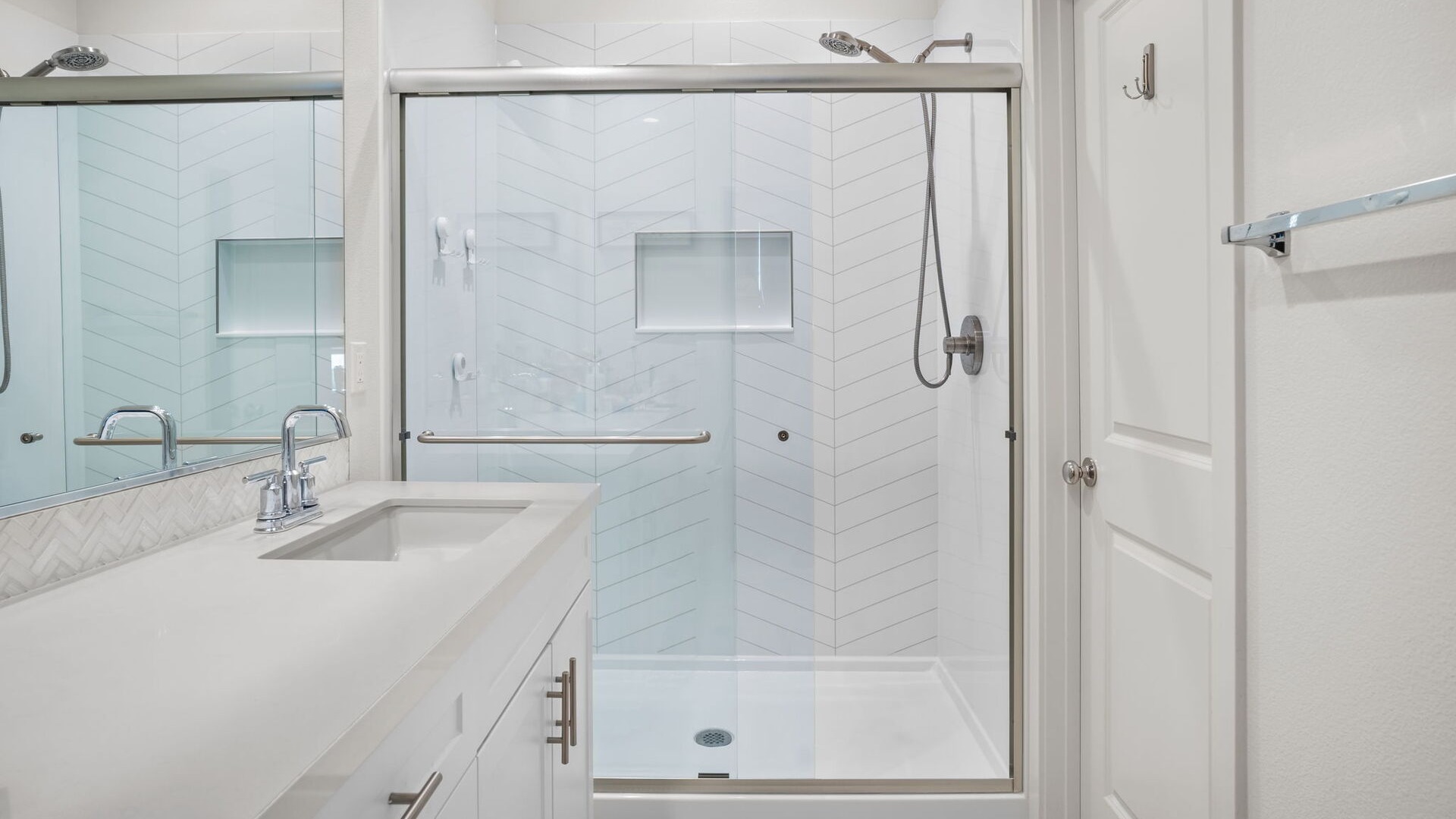A new walk-in shower with a handheld shower head, a shower niche, and clear sliding glass doors