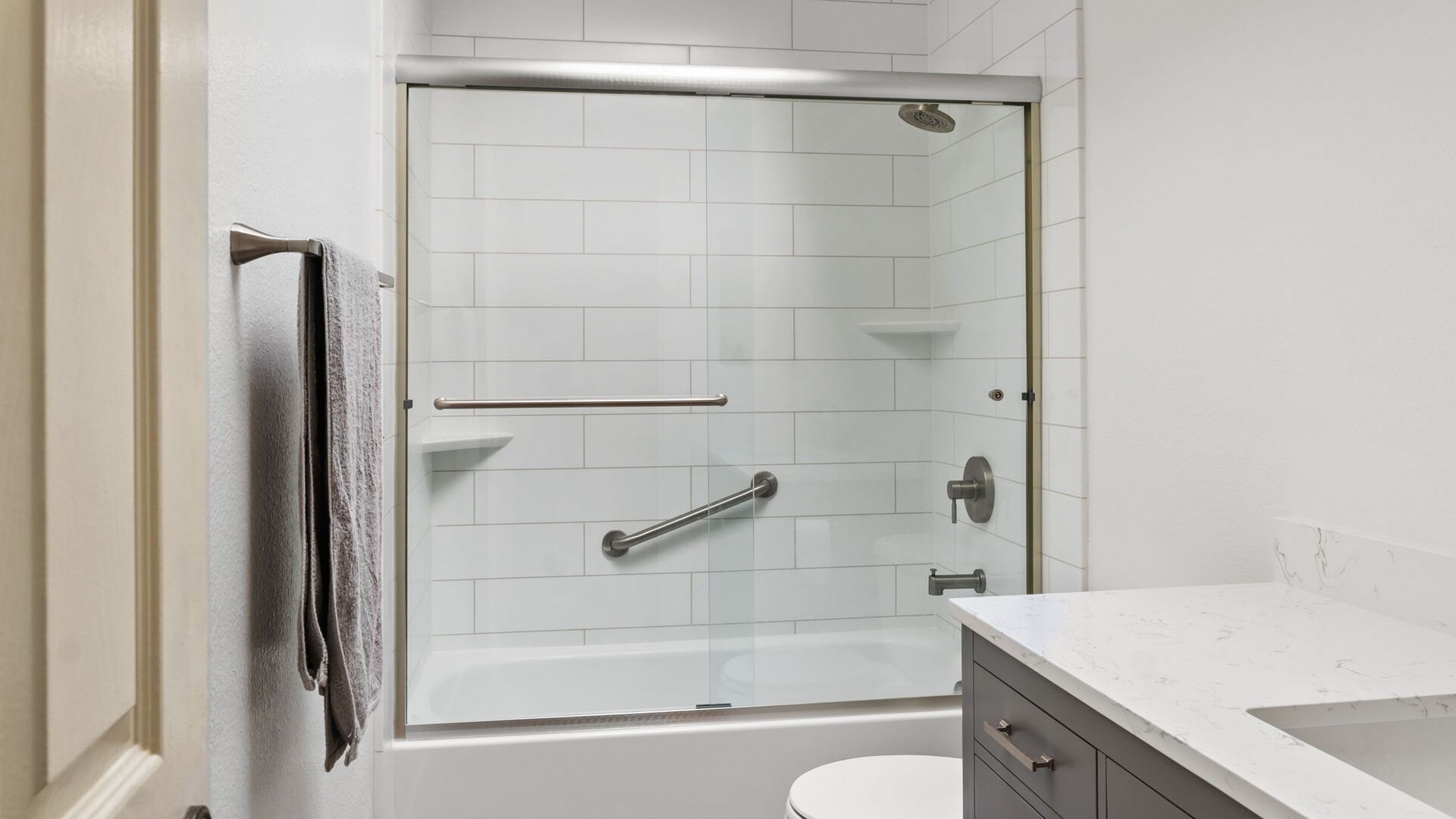 A grayline Fairfield patterned wall tub-and-shower combo with a grab bar, sliding glass door, and two corner shelves.