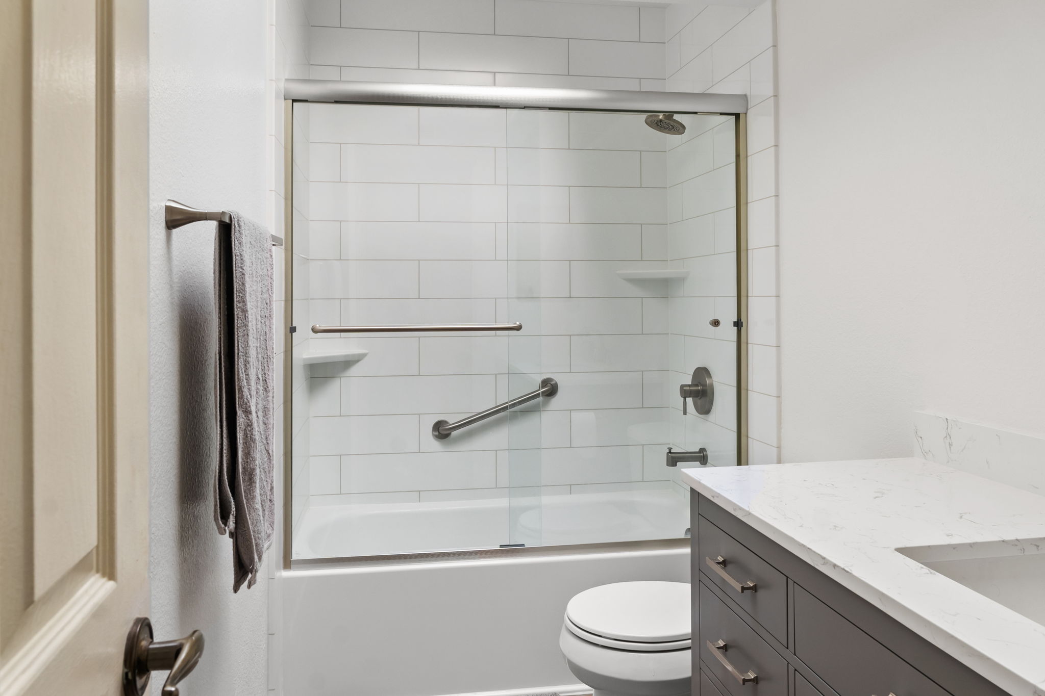 A bathroom with a new shower that has sliding glass doors, a grab bar, and two corner shelves.