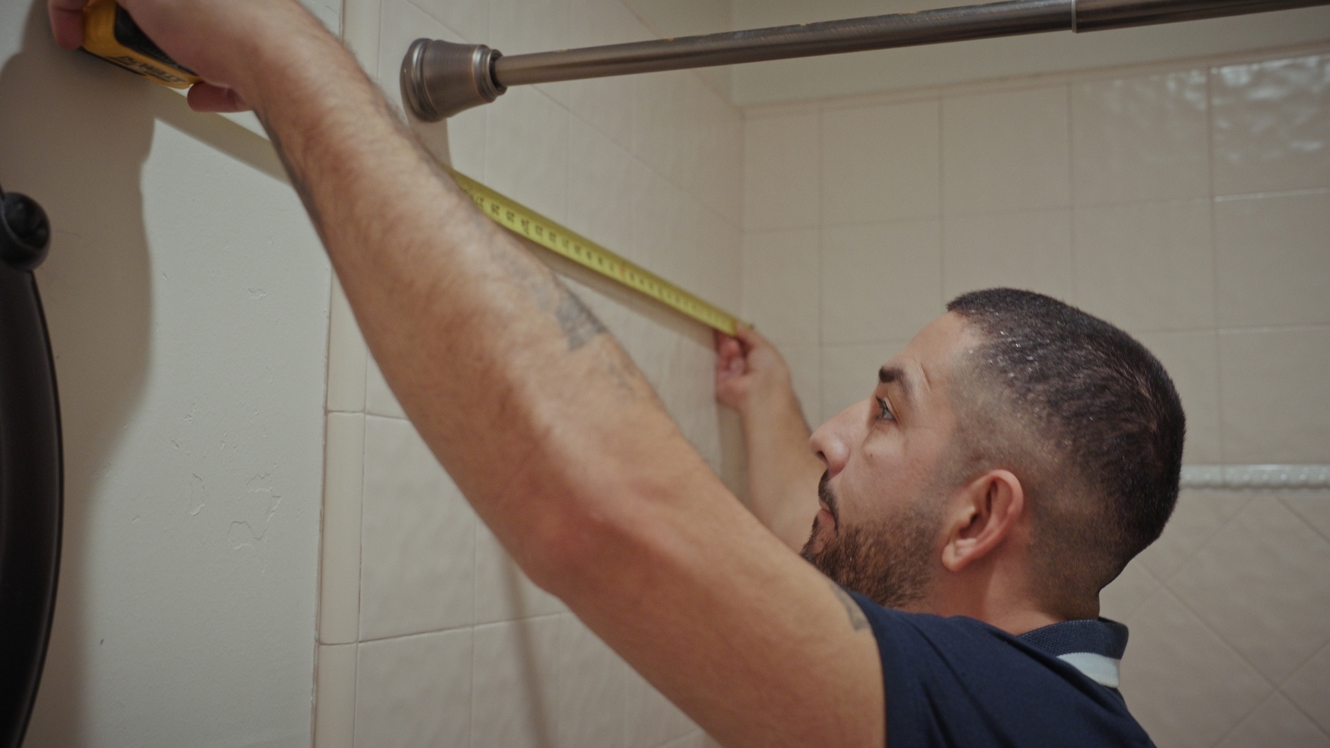 Design Consultant using a measuring tape on a wall, taking measurements in the tub and shower area.