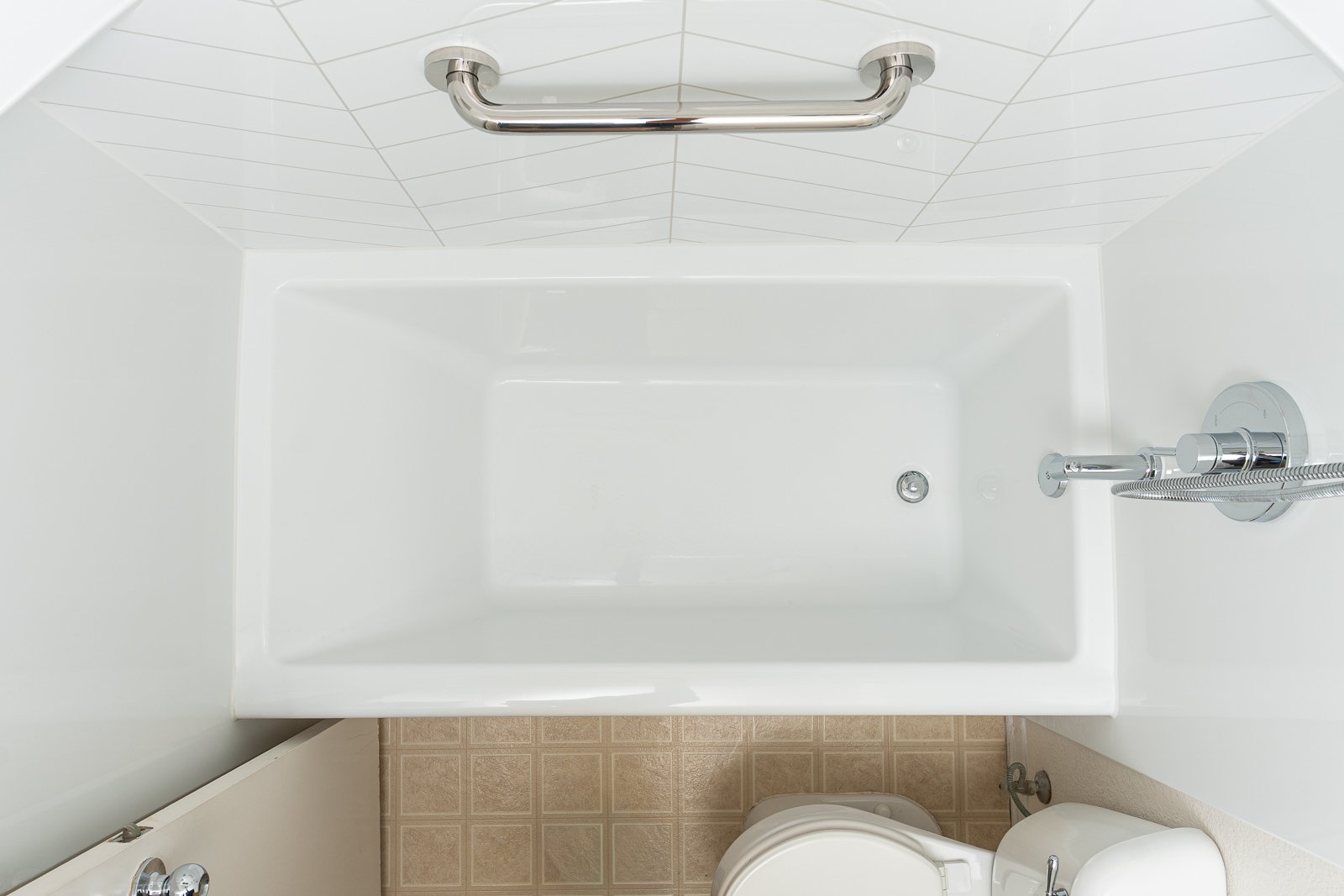A newly installed white tub with a grab bar on the shower wall above.