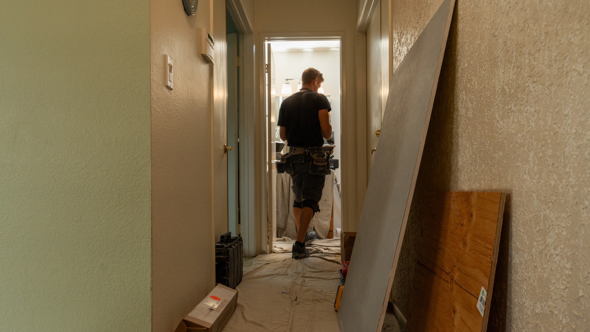 A photo of a hallway with mats on the ground to prevent bringing in dirt, with a shower installer specialist walking in a bathroom.