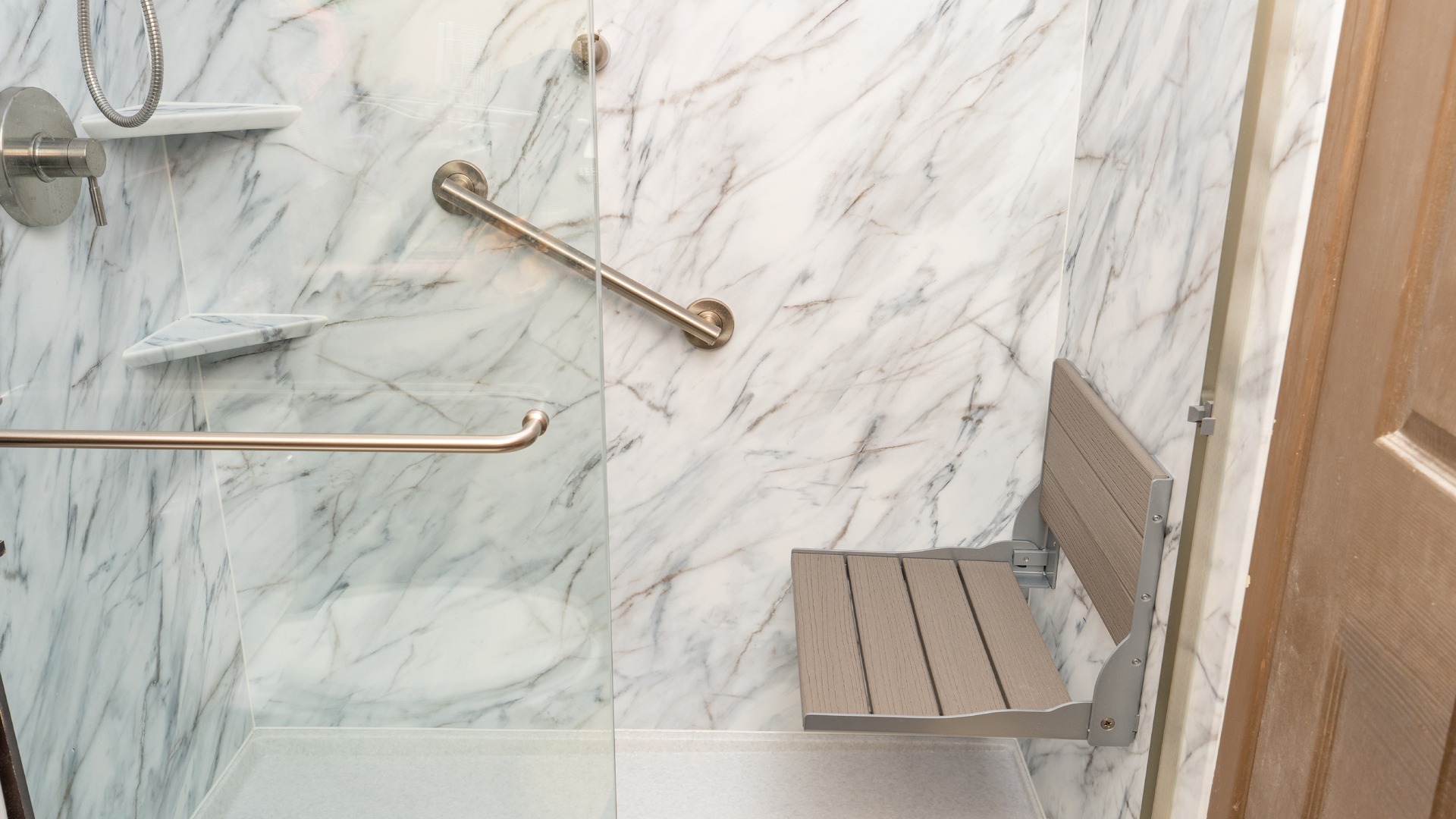 A walk-in shower remodel made for aging in place, with a foldable seat, a grab bar, and two corner shelves.