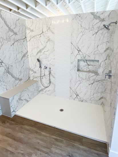 A Calcutta marble walk in shower with a handheld shower next to a custom seat, a storage niche, and a fixed shower head