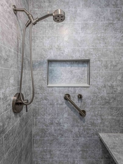 A walk-in shower with a handheld shower, a storage niche, a grab bar, and a shower bench.
