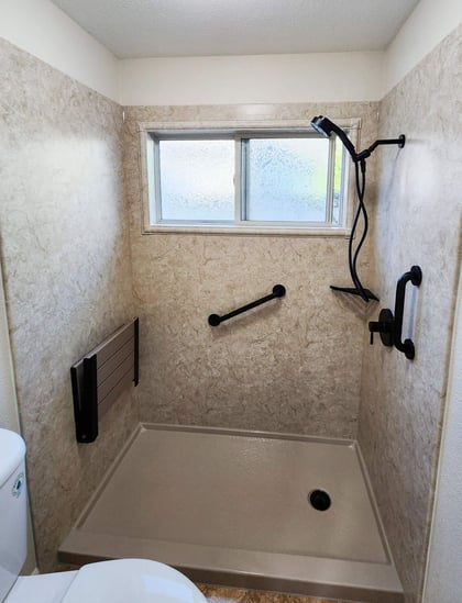 A remodeled walk-in shower with a handheld shower head, 2 grab bars, a corner shelf, and a foldable seat