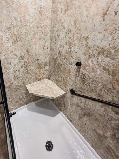 A remodeled walk-in shower with a grab bar and corner seat