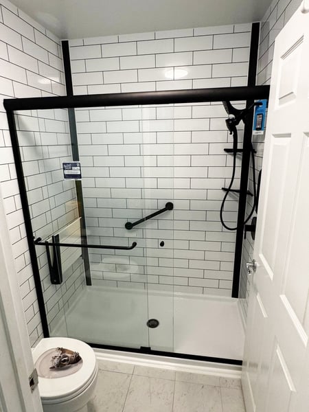 A remodeled walk-in shower with matte black finish, tile patterned walls, and a folding shower seat