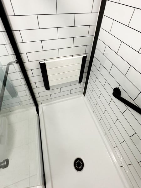 Inside of a remodeled walk-in shower with matte black finish, tile patterned walls, a grab bar, and a folding shower seat