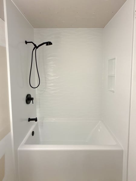 Remodeled tub and shower combo with scallop walls, a shower niche, and matte black finish