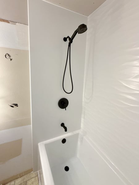A corner view of a remodeled tub and shower combo with scallop walls, a shower niche, and matte black finish