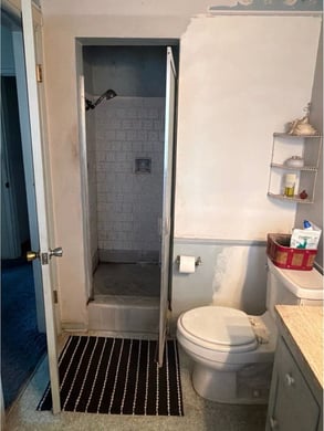 A bathroom with a door open to reveal a tightly spaced walk-in cave shower