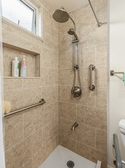 A walk-in shower with a shower niche, two grab bars, a handheld-rain shower head combo, all with a brushed nickel finish