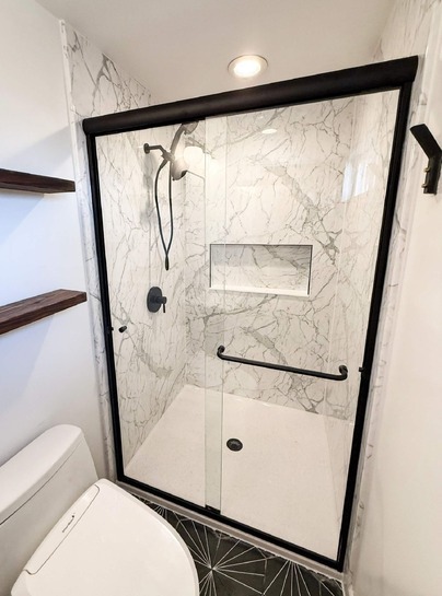 A calcutta marble BP-Cor2 shower wall with clear sliding glass doors, a shower niche and a handheld-fixed shower head combo