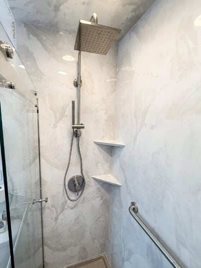 A new walk-in shower with a rain-handheld shower head combo, clear glass doors, a grab bar, and two corner storage shelves.