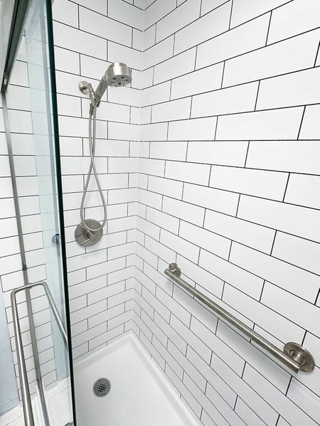 A walk in shower with a handheld shower head, clear glass doors, and a grab bar