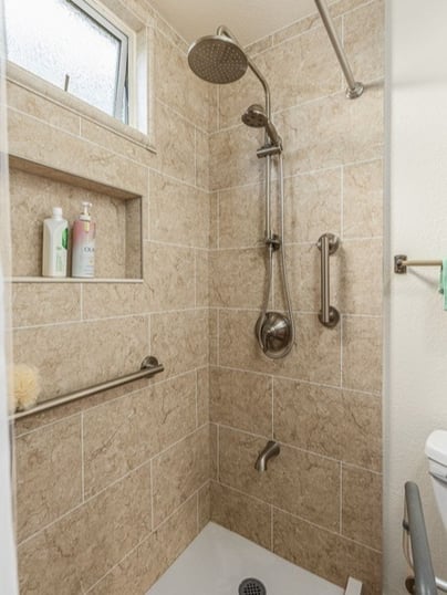 A new walk-in shower with a handheld-rain shower head, two grab bars with a brushed nickel finish, and a storage niche.