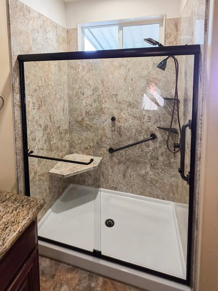 A walk-in shower with two grab bars, a corner seat, two corner storage and a handheld-fixed shower head combo