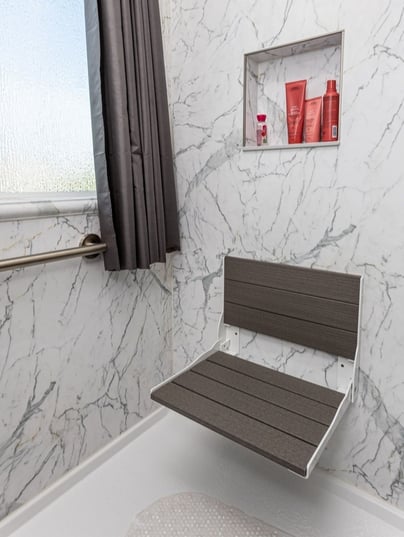 A remodeled shower with a composite seat and a shower niche holding shampoo bottles above it