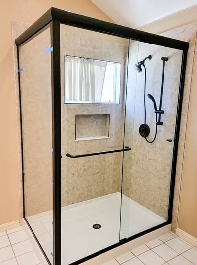 A shower remodel with clear sliding glass doors, a shower storage niche, and a fixed and hose shower head combo.